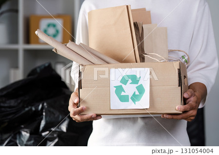 Young man holding a box of recycled materials, promoting eco-friendly practices in sustainable living environment. Young man holding a box of recycled materials, promoting eco-friendly practices in sustainable living environment. 131054004