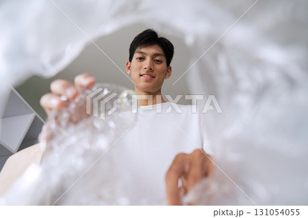 Young man smiling while recycling plastic waste, demonstrating commitment to environmental sustainability. 131054055