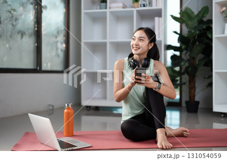 Happy woman enjoying fitness routine, using phone and water bottle during home workout. 131054059