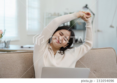 Diverse businesswoman stretching and relieving tension while working on her laptop at home, promoting wellness and self-care. 131054096