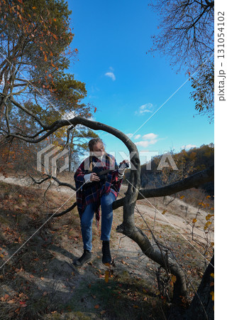 Blonde woman playing guitar ukulele outdoors in autumn forest. Concept of sound therapy, mental health and wellness rituals. Calmness tranquility audio-sensory practices. Aura farming Blonde woman playing guitar ukulele outdoors in autumn forest. Concept of sound therapy, mental health and wellness rituals. Calmness tranquility audio-sensory practices. Aura farming 131054102