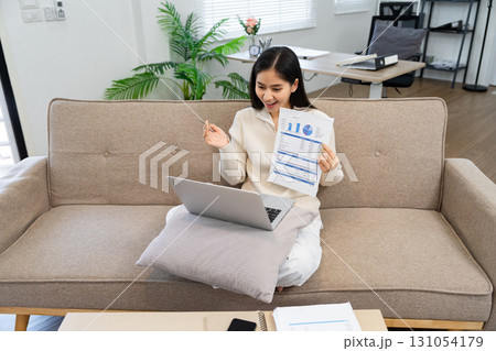 Young professional reviewing documents and discussing strategies on a video call, showcasing remote work efficiency. 131054179