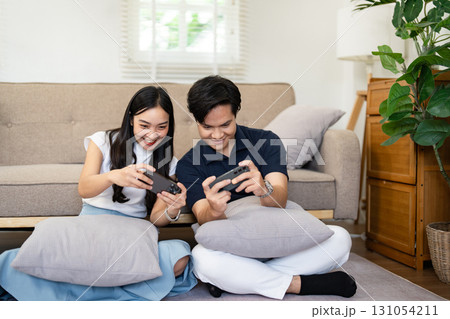 Couple gaming on the floor in a cozy living room, sharing laughter and playful competition. 131054211