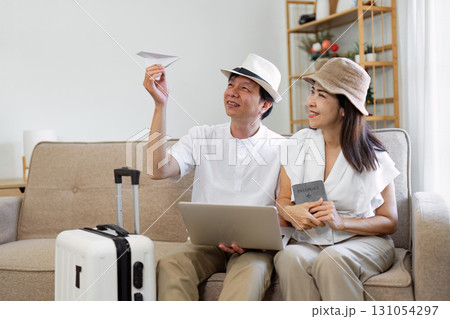 Elderly Asian couple joyfully planning their trip with a laptop and passport, while playfully tossing a paper airplane. 131054297