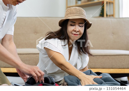 Focused Asian woman organizing clothes while packing for a trip, demonstrating travel preparation skills. 131054464