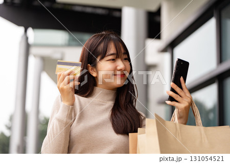 Young woman shopping with smartphone and credit card, expressing excitement outside a modern store Young woman shopping with smartphone and credit card, expressing excitement outside a modern store 131054521