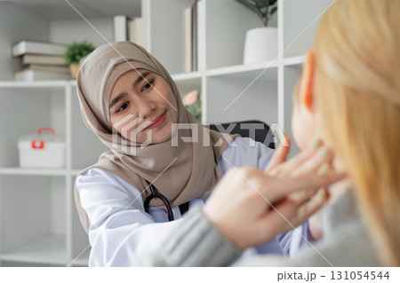 Compassionate female doctor in hijab examining a patient's ear in a modern healthcare setting. 131054544