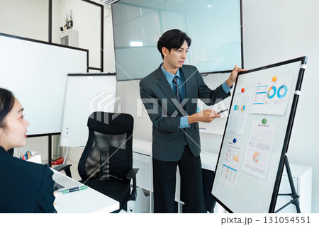 Dynamic Asian businessman presenting analytical data to a team during a meeting in a modern office. Dynamic Asian businessman presenting analytical data to a team during a meeting in a modern office. 131054551