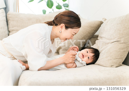 ソファで赤ちゃんをあやす若いアジア人女性（母親,育児,子育て） 131056329
