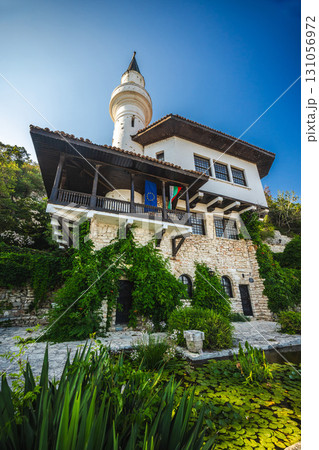 Balchik Palace in Bulgaria with stone walls, a minaret tower, EU and Bulgarian flags, and lush greenery by a pond with water lilies. 131056972