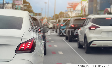 Rear side of white car and turn on brake light. Traffic is congested and there are long queues in the city. Blurred image of traffic jam with town under the blue sky. 131057793