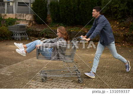 Happy young couple having fun with shopping cart outdoors in autumn park, wearing stylish casual outfits with denim and flannel, laughing and enjoying joyful moment, surrounded by autumn foliage and Happy young couple having fun with shopping cart outdoors in autumn park, wearing stylish casual outfits with denim and flannel, laughing and enjoying joyful moment, surrounded by autumn foliage and 131059337