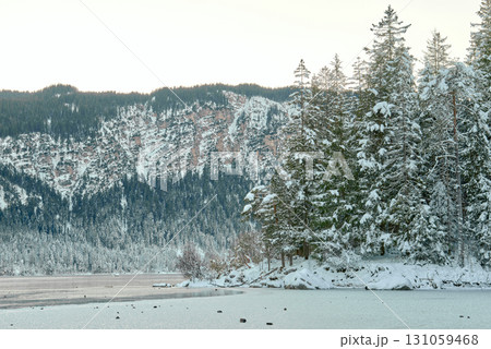 A picturesque evening landscape view of the frozen Eibsee lake at the foot of the Zugspitze mountain, showcasing a serene winter scene with snow-covered pine trees, a snowy forest. Twilight Alpine A picturesque evening landscape view of the frozen Eibsee lake at the foot of the Zugspitze mountain, showcasing a serene winter scene with snow-covered pine trees, a snowy forest. Twilight Alpine 131059468