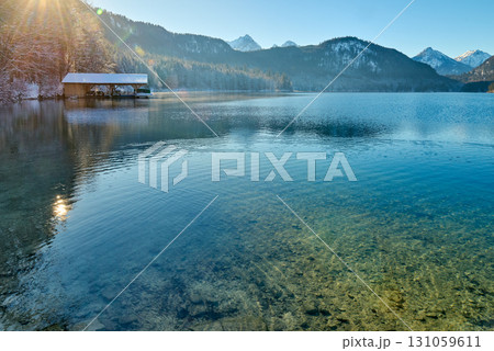 Serene Winter Wonderland: Frozen Lake Reflects Snow-Capped Mountains in Golden Morning Light Pristine Icy Landscape Captures Breathtaking Beauty of Alpine Lake on Crisp Sunny Day 131059611