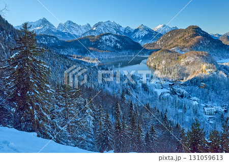 Snowy Mountain Landscape with Iconic Castle Overlooking Serene Lake and Alpine Peaks in Ethereal Winter Wonderland Bathed in Soft Dawn Light 131059613
