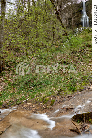 Serene Forest Waterfall with Wooden Bridge and Observers in Lush Greenery. Serene Forest Waterfall with Wooden Bridge and Observers in Lush Greenery. 131059623