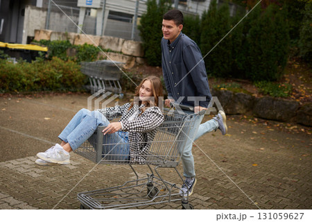 Happy young couple having fun with a shopping cart outdoors in autumn park, wearing stylish casual outfits with denim and flannel, laughing and enjoying the moment. 131059627