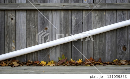 Colorful autumn leaves scattered under a white pipe against a wooden fence background 131059888