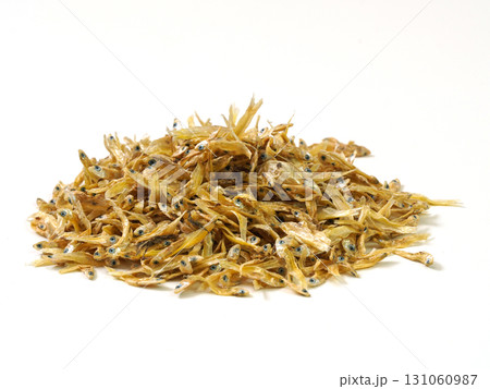 Pile of dried small fish, golden-brown in color, arranged on white background 131060987