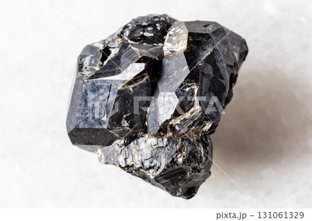 unpolished black andradite garnet on white marble unpolished black andradite garnet on white marble 131061329