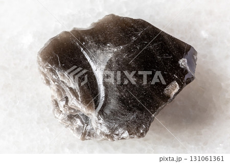 sample of rough obsidian rock on white marble 131061361