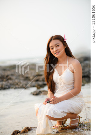 A woman in a white dress is enjoying her vacation on the beach with a retro camera in hand. A woman in a white dress is enjoying her vacation on the beach with a retro camera in hand. 131061656