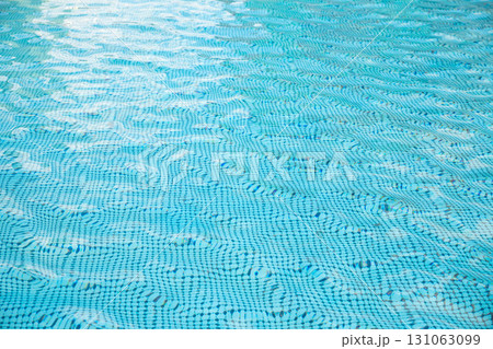 Bright blue water fills a swimming pool, with gentle ripples reflecting sunlight. The surface invites relaxation and leisure activities during a warm day. 131063099