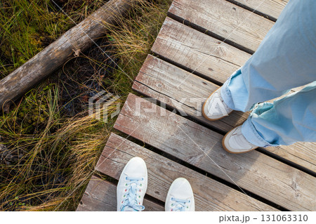 Two pairs of sneakers on wooden walkway on marshy wetland with green grass and aquatic plant life on sunny day. top view 131063310