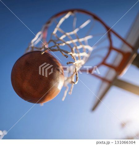 Basketball hoop with ball about to go through net against clear blue sky, captured from below with sunlight shining brightly 131066304
