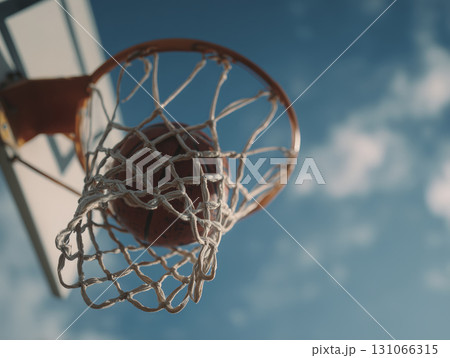 Basketball going through net of basketball hoop on sunny day with blue sky and clouds 131066315