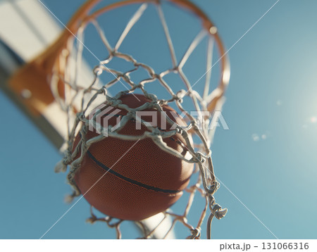 Basketball going through net of basketball hoop outdoors under clear blue sky, capturing moment of scoring with sunlight shining brightly 131066316