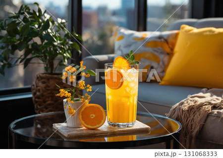 glass of orange juice and sliced oranges on table in the room, modern interior with sofa and pillows, beautiful view outside window of modern metropolis with skyscrapers glass of orange juice and sliced oranges on table in the room, modern interior with sofa and pillows, beautiful view outside window of modern metropolis with skyscrapers 131068333