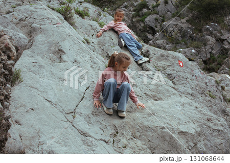 two little girls sisters twins climbing on rock together outside, lifestyle people concept 131068644