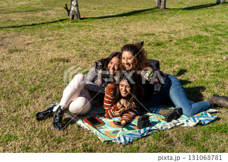 Three latin girls having fun and enjoying a picnic in the park Three latin girls having fun and enjoying a picnic in the park 131068781