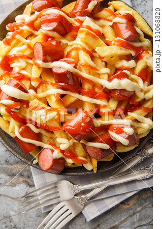 Fast food salchipapa is a mix of sliced hot dogs and french fries closeup on the plate on the table. Vertical top view 131068820