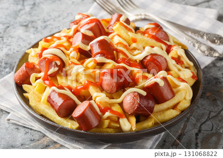 Salchipapas is a South American and Caribbean fast food dish consisting of thinly sliced pan-fried beef sausages and French fries closeup on the plate. Horizontal 131068822