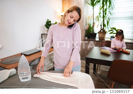 Busy mother multitasking with phone call while ironing clothes at home 131069157