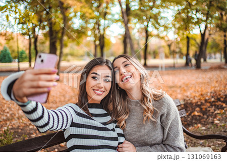 Two girls capture moments of joy together in a colorful autumn park Two girls capture moments of joy together in a colorful autumn park 131069163
