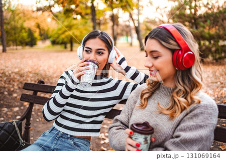 Two girls enjoy autumn vibes while sipping warm drinks in the park 131069164