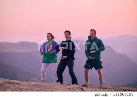Group of people practicing Tai Chi outdoors at sunrise on mountain, performing slow meditative movements for balance, energy, health, and mindfulness in nature 131069189