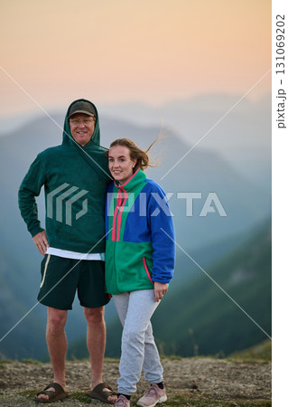 Happy couple posing outdoors on mountain at sunset, dressed in casual colorful hoodies, smiling and enjoying nature, travel, lifestyle, and togetherness in a scenic landscape Happy couple posing outdoors on mountain at sunset, dressed in casual colorful hoodies, smiling and enjoying nature, travel, lifestyle, and togetherness in a scenic landscape 131069202