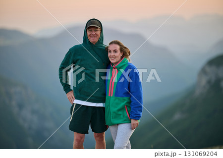 Happy couple posing outdoors on mountain at sunset, dressed in casual colorful hoodies, smiling and enjoying nature, travel, lifestyle, and togetherness in a scenic landscape 131069204