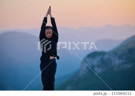 Woman practicing Tai Chi in traditional black outfit on mountain at sunrise, arms outstretched in meditation pose focusing on balance, energy, and mindfulness in nature. 131069212
