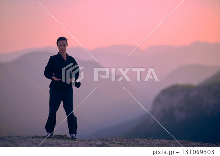 Woman practicing Tai Chi in traditional black outfit on mountain at sunrise, arms outstretched in meditation pose focusing on balance, energy, and mindfulness in nature. 131069303