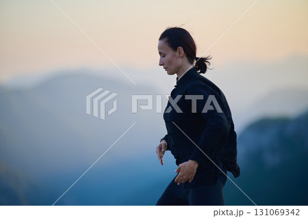 Woman practicing Tai Chi in traditional black outfit on mountain at sunrise, arms outstretched in meditation pose focusing on balance, energy, and mindfulness in nature. 131069342