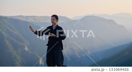 Woman practicing Tai Chi in traditional black outfit on mountain at sunrise, arms outstretched in meditation pose focusing on balance, energy, and mindfulness in nature. Woman practicing Tai Chi in traditional black outfit on mountain at sunrise, arms outstretched in meditation pose focusing on balance, energy, and mindfulness in nature. 131069488