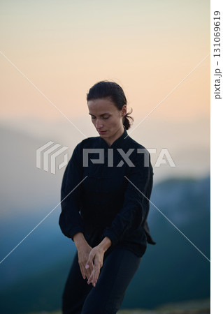 Woman practicing Tai Chi in traditional black outfit on mountain at sunrise, arms outstretched in meditation pose focusing on balance, energy, and mindfulness in nature. Woman practicing Tai Chi in traditional black outfit on mountain at sunrise, arms outstretched in meditation pose focusing on balance, energy, and mindfulness in nature. 131069619