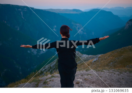 Woman practicing Tai Chi in traditional black outfit on mountain at sunrise, arms outstretched in meditation pose focusing on balance, energy, and mindfulness in nature. Woman practicing Tai Chi in traditional black outfit on mountain at sunrise, arms outstretched in meditation pose focusing on balance, energy, and mindfulness in nature. 131069635