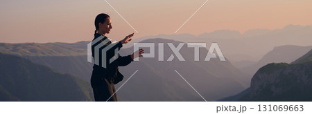 Woman practicing Tai Chi in traditional black outfit on mountain at sunrise, arms outstretched in meditation pose focusing on balance, energy, and mindfulness in nature. 131069663