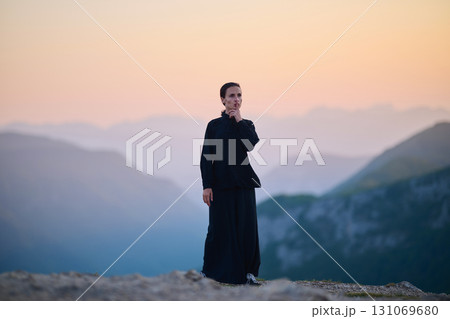 Woman practicing Tai Chi in traditional black outfit on mountain at sunrise, arms outstretched in meditation pose focusing on balance, energy, and mindfulness in nature. 131069680